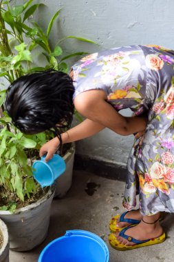 Şirin 5 yaşındaki Asyalı küçük kız, ev balkonundaki saksıları suluyor, bitkileri sularken doğa anaya duyulan sevgi, çocuk yetiştirme.