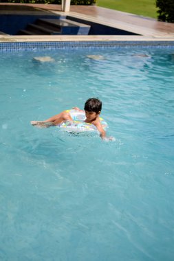 Havuzda yüzen mutlu Hintli çocuk, sıcak yaz tatillerinde hava tüpüyle birlikte yüzen çocuk, büyük bir havuzda yüzen çocuk..