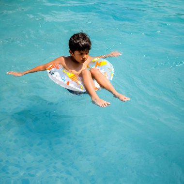 Havuzda yüzen mutlu Hintli çocuk, sıcak yaz tatillerinde hava tüpüyle birlikte yüzen çocuk, büyük bir havuzda yüzen çocuk..