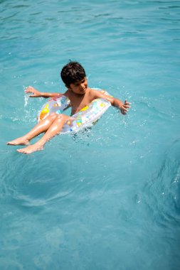 Havuzda yüzen mutlu Hintli çocuk, sıcak yaz tatillerinde hava tüpüyle birlikte yüzen çocuk, büyük bir havuzda yüzen çocuk..