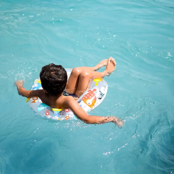 Happy Indian boy swimming in a pool, Kid wearing swimming costume along with air tube during hot summer vacations, Children boy in big swimming pool.