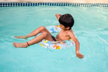 Havuzda yüzen mutlu Hintli çocuk, sıcak yaz tatillerinde hava tüpüyle birlikte yüzen çocuk, büyük bir havuzda yüzen çocuk..