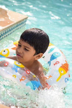 Havuzda yüzen mutlu Hintli çocuk, sıcak yaz tatillerinde hava tüpüyle birlikte yüzen çocuk, büyük bir havuzda yüzen çocuk..