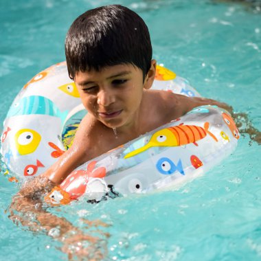 Havuzda yüzen mutlu Hintli çocuk, sıcak yaz tatillerinde hava tüpüyle birlikte yüzen çocuk, büyük bir havuzda yüzen çocuk..
