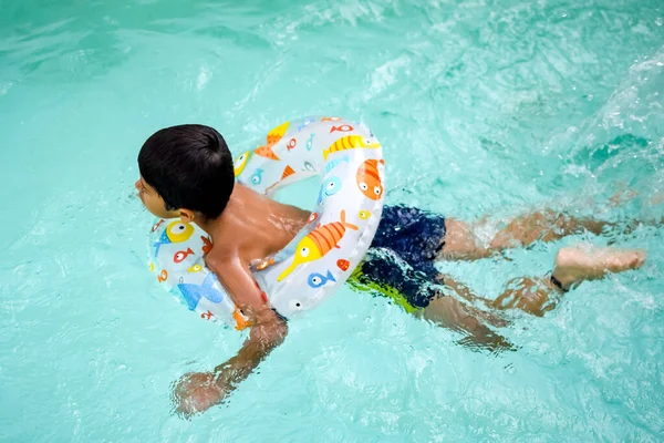Happy Indian boy swimming in a pool, Kid wearing swimming costume along with air tube during hot summer vacations, Children boy in big swimming pool.