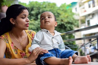 Sevgi dolu anne bebeğini balkonda taşıyor. Mutlu bir annenin parlak portresi. Çocuğu elinde tutuyor. Anne ve 1 yaşındaki küçük oğlu..