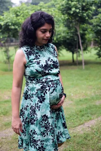 A pregnant Indian lady poses for outdoor pregnancy shoot and hands on  belly, Indian pregnant woman