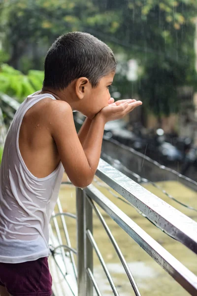 Little kid playing in summer rain in house balcony, Indian smart boy playing with rain drops during monsoon rainy season, kid playing in rain
