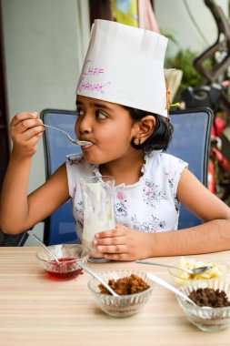 Tatlı Hintli aşçı kız vanilyalı dondurma, browni, kakao tozu, taze doğranmış meyve ve çilek şurubu içeren ateşte pişirilmemiş dondurma yemeğinin bir parçası olarak sundae hazırlıyor. Küçük çocuk yemek hazırlıyor.
