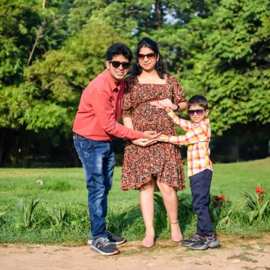 Hintli çift 5 yaşındaki çocuklarıyla hamilelik çekimleri için poz veriyor. Çift yeşil çimenli bir çimenlikte poz veriyor ve kadın Yeni Delhi, Hindistan 'daki Lodhi Garden' da bebeğiyle hava atıyor.