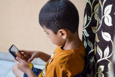 Evde cep telefonu kullanan Asyalı mutlu küçük çocuğun portresi. Küçük çocuk elinde cep telefonu tutuyor, internetten okul konseptine geri dönüyor. Çevrimiçi Sınıf kavramı