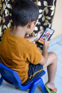 Evde cep telefonu kullanan Asyalı mutlu küçük çocuğun portresi. Küçük çocuk elinde cep telefonu tutuyor, internetten okul konseptine geri dönüyor. Çevrimiçi Sınıf kavramı