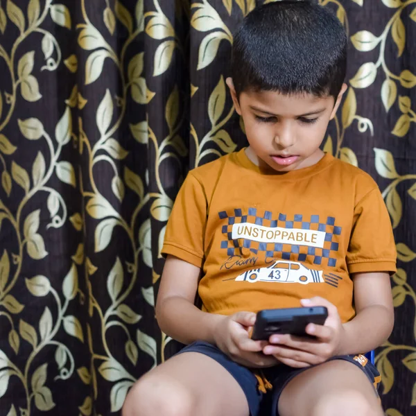 Evde cep telefonu kullanan Asyalı mutlu küçük çocuğun portresi. Küçük çocuk elinde cep telefonu tutuyor, internetten okul konseptine geri dönüyor. Çevrimiçi Sınıf kavramı