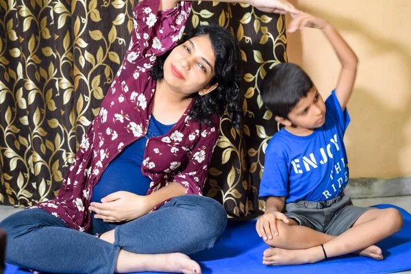 Pregnant woman doing Pregnancy yoga pose comfortable at home with her kid, Pregnant woman practicing simple yoga steps at home along with her son, Pregnancy yoga and fitness poses