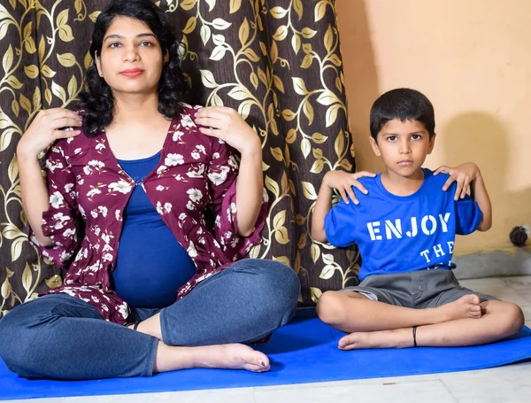 Pregnant woman doing Pregnancy yoga pose comfortable at home with her kid, Pregnant woman practicing simple yoga steps at home along with her son, Pregnancy yoga and fitness poses