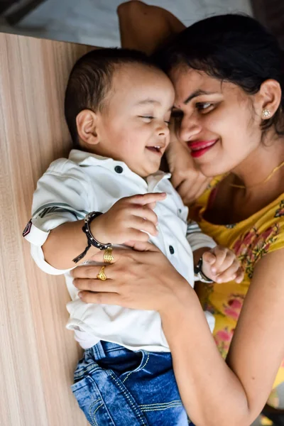 愛する母親は自宅のバルコニーで赤ちゃんを運ぶ 子供を抱えている幸せな母親の明るい肖像画 彼女の小さな1歳の息子と母 ロイヤリティフリーのストック画像