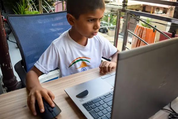 小学校1年生のオンライン授業のためにノートパソコンを使ってテーブルに座っている男の子 遠隔学習のために自宅からノートパソコンで勉強する子供オンライン教育 学校の男の子の子供のライフスタイルの概念 ストック画像