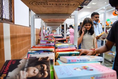 Delhi, Hindistan, Eylül 09 2023 - Çeşitli yaş grupları Delhi Uluslararası Kitap Fuarı 'ndaki bir kitaplığın içinde çeşitli kitaplar okuyor, Yıllık Kitap Fuarı' nda kitap seçimleri