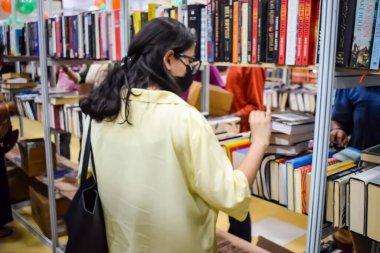 Delhi, Hindistan, Eylül 09 2023 - Çeşitli yaş grupları Delhi Uluslararası Kitap Fuarı 'ndaki bir kitaplığın içinde çeşitli kitaplar okuyor, Yıllık Kitap Fuarı' nda kitap seçimleri