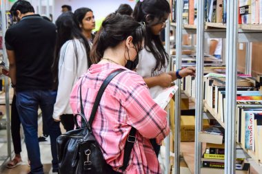 Delhi, Hindistan, Eylül 09 2023 - Çeşitli yaş grupları Delhi Uluslararası Kitap Fuarı 'ndaki bir kitaplığın içinde çeşitli kitaplar okuyor, Yıllık Kitap Fuarı' nda kitap seçimleri