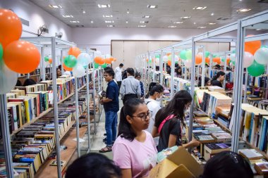Delhi, Hindistan, Eylül 09 2023 - Çeşitli yaş grupları Delhi Uluslararası Kitap Fuarı 'ndaki bir kitaplığın içinde çeşitli kitaplar okuyor, Yıllık Kitap Fuarı' nda kitap seçimleri