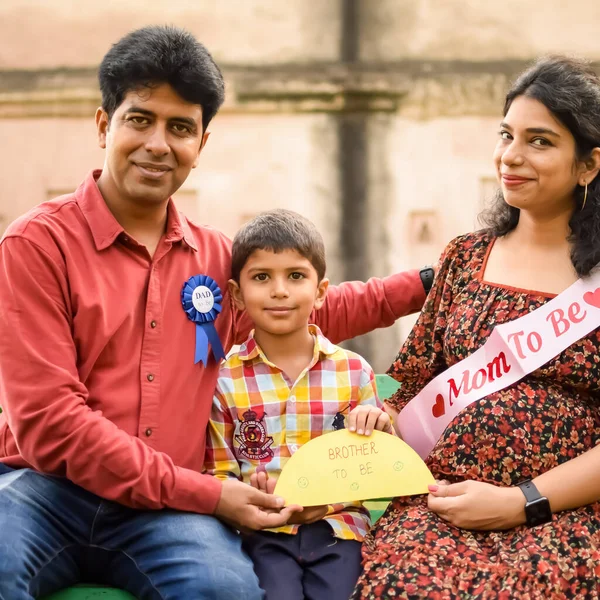 Indian couple posing for maternity baby shoot with their 5 year old kid. The couple is posing in a lawn with green grass and the woman is flaunting her baby bump in Lodhi Garden in New Delhi, India
