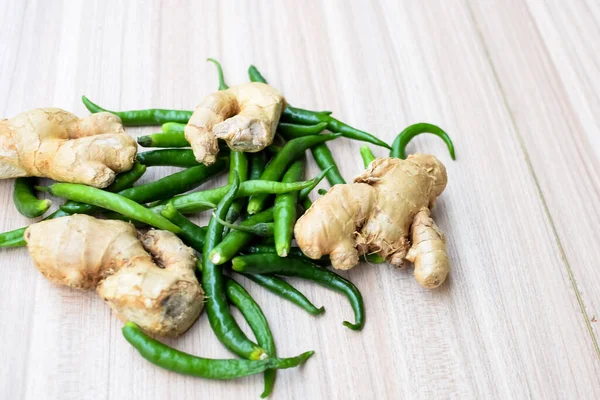 Fresh Ginger and green chili pepper on plain wooden table, green essential vegetables for all essential foods, view of unpeeled vegetables with plain background