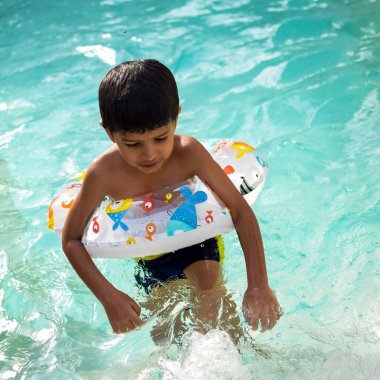 Havuzda yüzen mutlu Hintli çocuk, sıcak yaz tatillerinde hava tüpüyle birlikte yüzen çocuk, büyük bir havuzda yüzen çocuk..