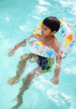 Havuzda yüzen mutlu Hintli çocuk, sıcak yaz tatillerinde hava tüpüyle birlikte yüzen çocuk, büyük bir havuzda yüzen çocuk..