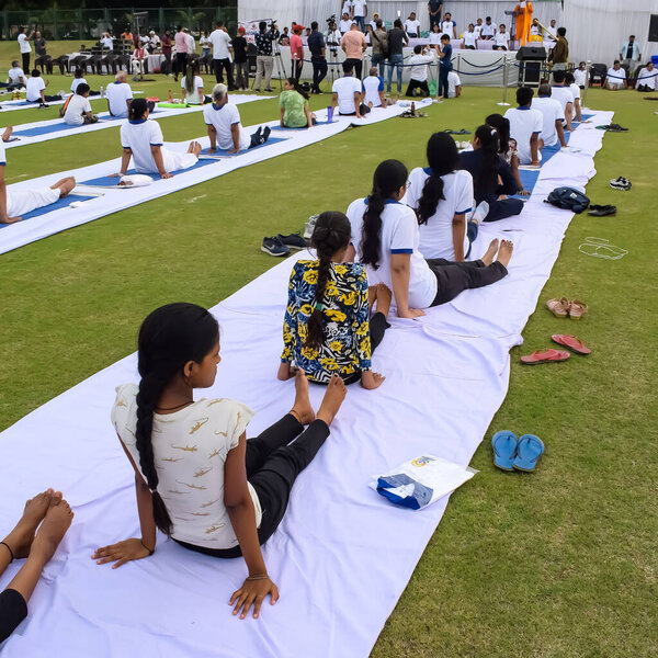 New Delhi, India, June 21, 2023 - Group Yoga exercise session for people at Yamuna Sports Complex in Delhi on International Yoga Day, Big group of adults attending yoga class in cricket stadium