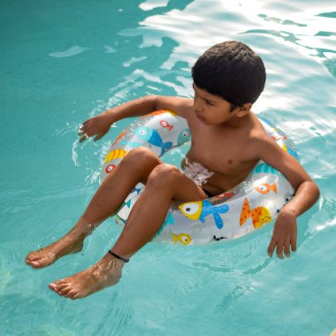 Havuzda yüzen mutlu Hintli çocuk, sıcak yaz tatillerinde hava tüpüyle birlikte yüzen çocuk, büyük bir havuzda yüzen çocuk..