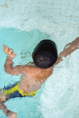 Havuzda yüzen mutlu Hintli çocuk, sıcak yaz tatillerinde hava tüpüyle birlikte yüzen çocuk, büyük bir havuzda yüzen çocuk..