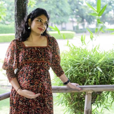 Hamile bir Hintli kadın hamilelik çekimleri için dışarıda poz veriyor ve ellerini karnının üstüne koyuyor, Hintli hamile kadın elini karnının üstüne koyuyor.