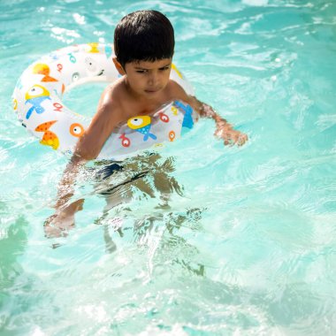 Havuzda yüzen mutlu Hintli çocuk, sıcak yaz tatillerinde hava tüpüyle birlikte yüzen çocuk, büyük bir havuzda yüzen çocuk..