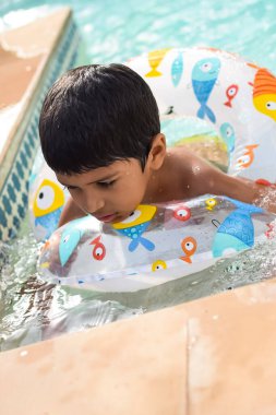 Havuzda yüzen mutlu Hintli çocuk, sıcak yaz tatillerinde hava tüpüyle birlikte yüzen çocuk, büyük bir havuzda yüzen çocuk..
