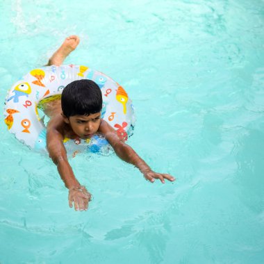 Havuzda yüzen mutlu Hintli çocuk, sıcak yaz tatillerinde hava tüpüyle birlikte yüzen çocuk, büyük bir havuzda yüzen çocuk..
