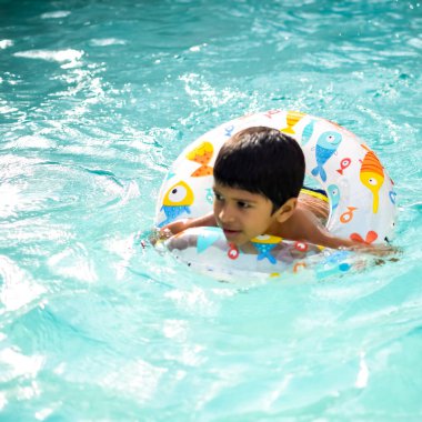 Havuzda yüzen mutlu Hintli çocuk, sıcak yaz tatillerinde hava tüpüyle birlikte yüzen çocuk, büyük bir havuzda yüzen çocuk..