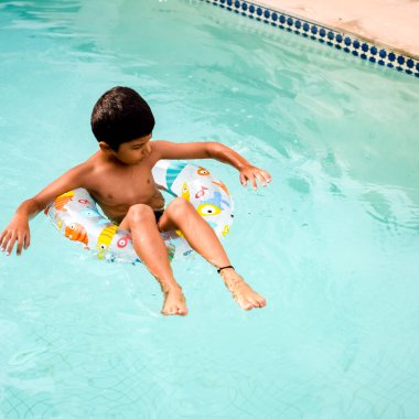 Havuzda yüzen mutlu Hintli çocuk, sıcak yaz tatillerinde hava tüpüyle birlikte yüzen çocuk, büyük bir havuzda yüzen çocuk..