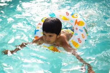 Havuzda yüzen mutlu Hintli çocuk, sıcak yaz tatillerinde hava tüpüyle birlikte yüzen çocuk, büyük bir havuzda yüzen çocuk..