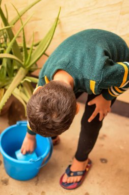 Şirin 5 yaşındaki Asyalı çocuk, ev balkonundaki saksıları suluyor. Bitkileri sularken küçük tatlı bir çocuğun doğaya olan sevgisi.