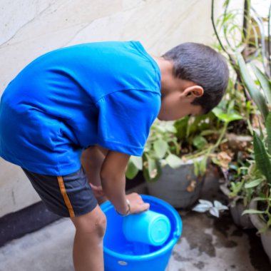 Şirin 5 yaşındaki Asyalı çocuk, ev balkonundaki saksıları suluyor. Bitkileri sularken küçük tatlı bir çocuğun doğaya olan sevgisi.