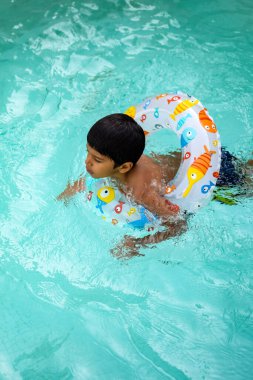Havuzda yüzen mutlu Hintli çocuk, sıcak yaz tatillerinde hava tüpüyle birlikte yüzen çocuk, büyük bir havuzda yüzen çocuk..
