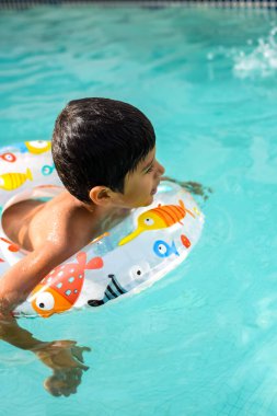 Havuzda yüzen mutlu Hintli çocuk, sıcak yaz tatillerinde hava tüpüyle birlikte yüzen çocuk, büyük bir havuzda yüzen çocuk..