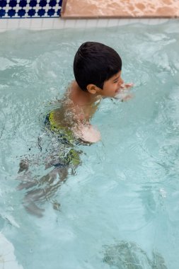 Havuzda yüzen mutlu Hintli çocuk, sıcak yaz tatillerinde hava tüpüyle birlikte yüzen çocuk, büyük bir havuzda yüzen çocuk..