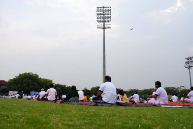 Yeni Delhi, Hindistan, 21 Haziran 2023 - Uluslararası Yoga Günü 'nde Delhi' deki Yamuna Spor Kompleksi 'nde grup Yoga egzersiz oturumu, kriket stadyumunda yoga derslerine katılan büyük bir grup yetişkin