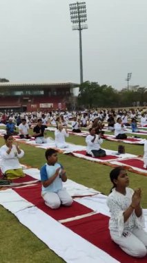 Yeni Delhi, Hindistan, 21 Haziran 2024 - Uluslararası Yoga Günü 'nde Delhi' deki Yamuna Spor Kompleksi 'nde grup Yoga egzersiz oturumu, kriket stadyumunda yoga sınıfına katılan büyük bir grup yetişkin