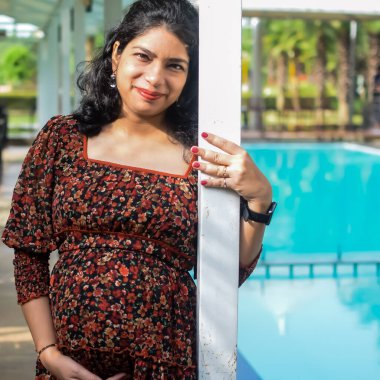 Hamile bir Hintli kadın hamilelik çekimleri için dışarıda poz veriyor ve ellerini karnının üstüne koyuyor, Hintli hamile kadın elini karnının üstüne koyuyor.