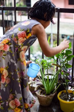 Şirin 5 yaşındaki Asyalı küçük kız, ev balkonundaki saksıları suluyor, bitkileri sularken doğa anaya duyulan sevgi, çocuk yetiştirme.