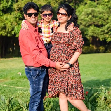 Hintli çift 5 yaşındaki çocuklarıyla hamilelik çekimleri için poz veriyor. Çift yeşil çimenli bir çimenlikte poz veriyor ve kadın Yeni Delhi, Hindistan 'daki Lodhi Garden' da bebeğiyle hava atıyor.