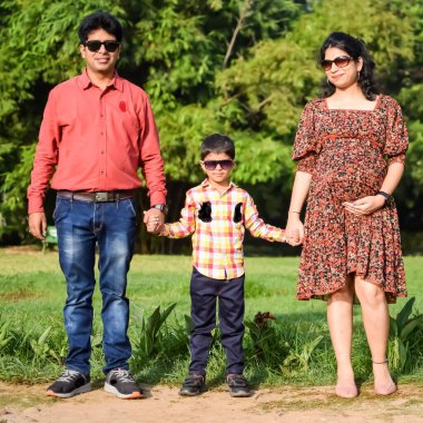 Hintli çift 5 yaşındaki çocuklarıyla hamilelik çekimleri için poz veriyor. Çift yeşil çimenli bir çimenlikte poz veriyor ve kadın Yeni Delhi, Hindistan 'daki Lodhi Garden' da bebeğiyle hava atıyor.